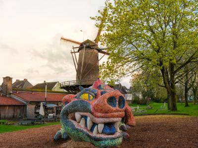 Eine Drachenfigur liegt auf dem Boden und im Hintergrund ist eine Mühle zu sehen.