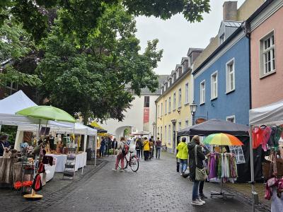 Straßenszene mit Marktständen und bunten Häusern bei bewölktem Himmel, Menschen bummeln und kaufen ein