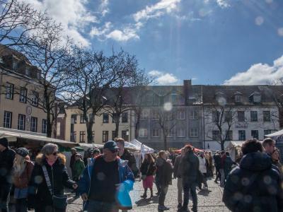 Menschen auf einem belebten Marktplatz bei sonnigem Wetter mit blauem Himmel und wenigen Wolken