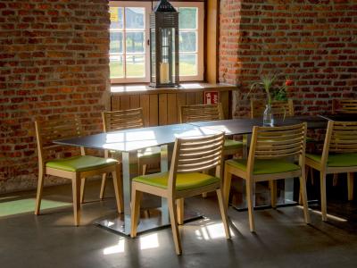 Innenansicht der Kaffeemühle. ein Tisch mit acht Stühlen ist zu sehen vor einer Backsteinmauer mit mittigem Fenster. Die Stühle haben ein hell grünes Sitzpolster. 