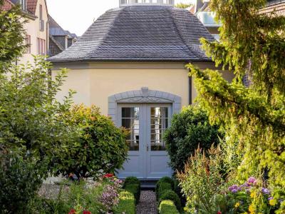 Auf dem Bild ist ein Garten Pavillon zu sehen. Rechts und links befinden sich grüne Bäume. es führt ein Weg gerade auf den Pavillon zu, der mit einer Hecke abgetrennt ist.