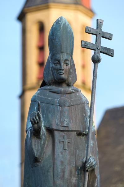 Statue des Heiligen Viktor mit Bischofsmütze und Kreuzstab vor unscharfem Kirchturm