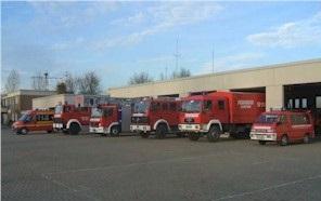 Mehrere rote Feuerwehrfahrzeuge vor einem Feuerwehrgebäude bei Tageslicht