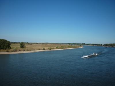 Breiter Fluss mit Frachtschiff, flache Uferlandschaft und klarer Himmel