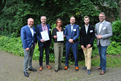Auf dem Bild stehen 6 Personen, zwei halten je ein Zettel in der Hand